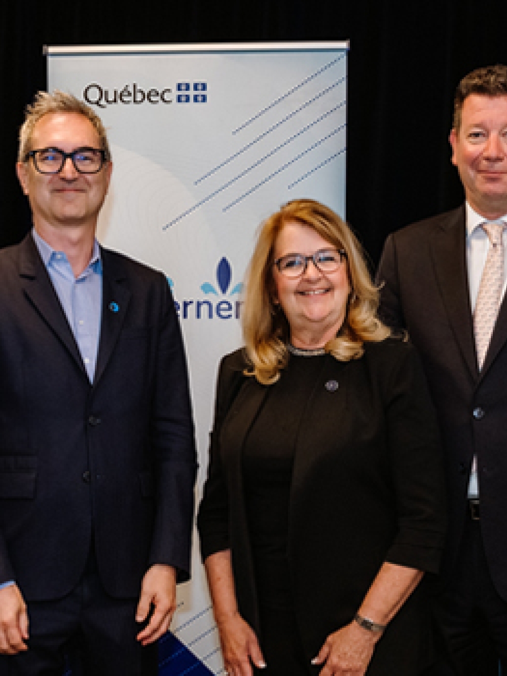 Groupe de personnes debout devant des panneaux portant les logos de Danone et du gouvernement du Québec, avec une table présentant des produits de yogourt Oikos au premier plan.