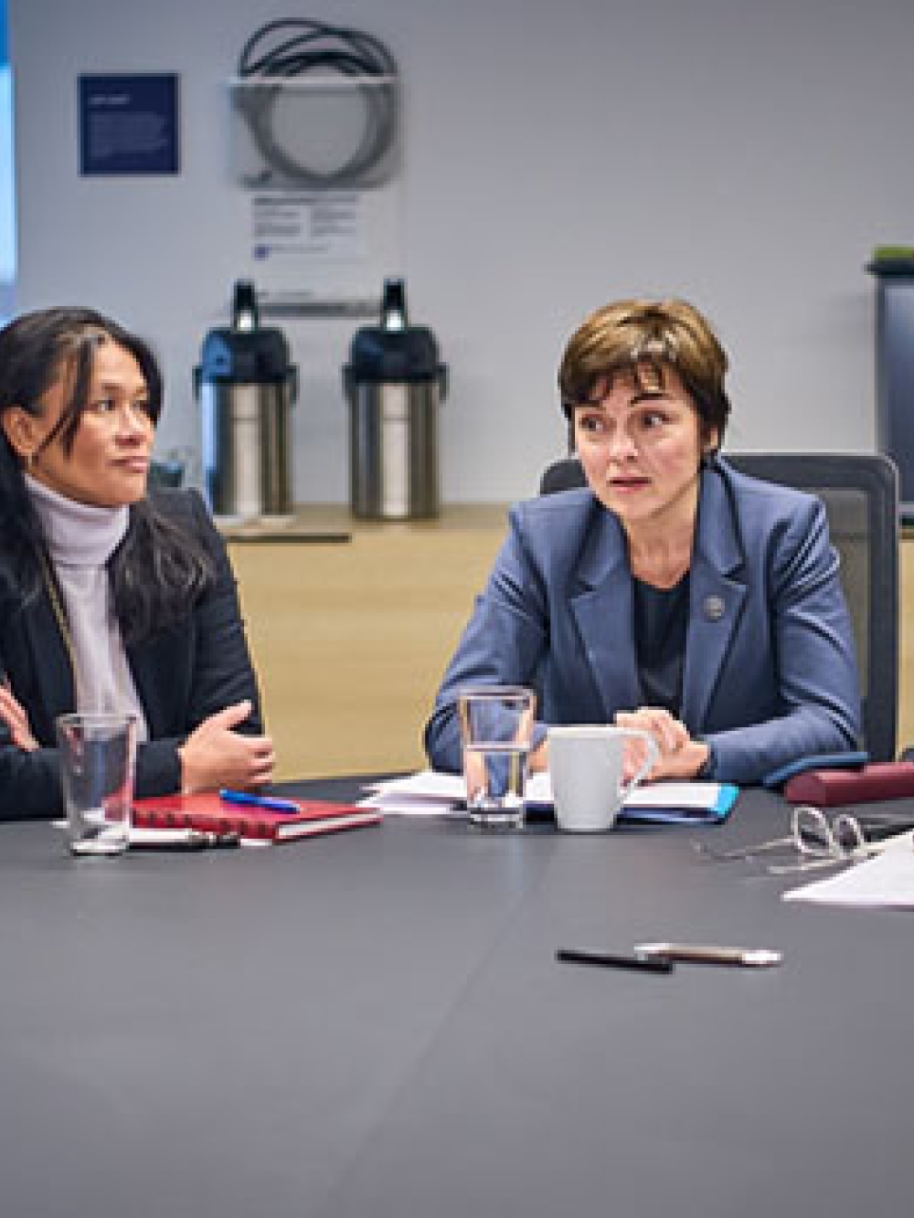 Personnes assises autour d’une grande table de réunion, discutant et prenant des notes lors d’un échange formel dans une salle de conférence.