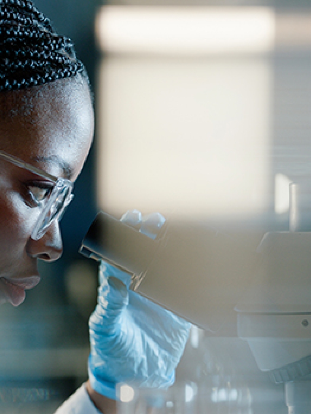 Personne en laboratoire observant un échantillon au microscope, avec des éléments d’équipement scientifique.