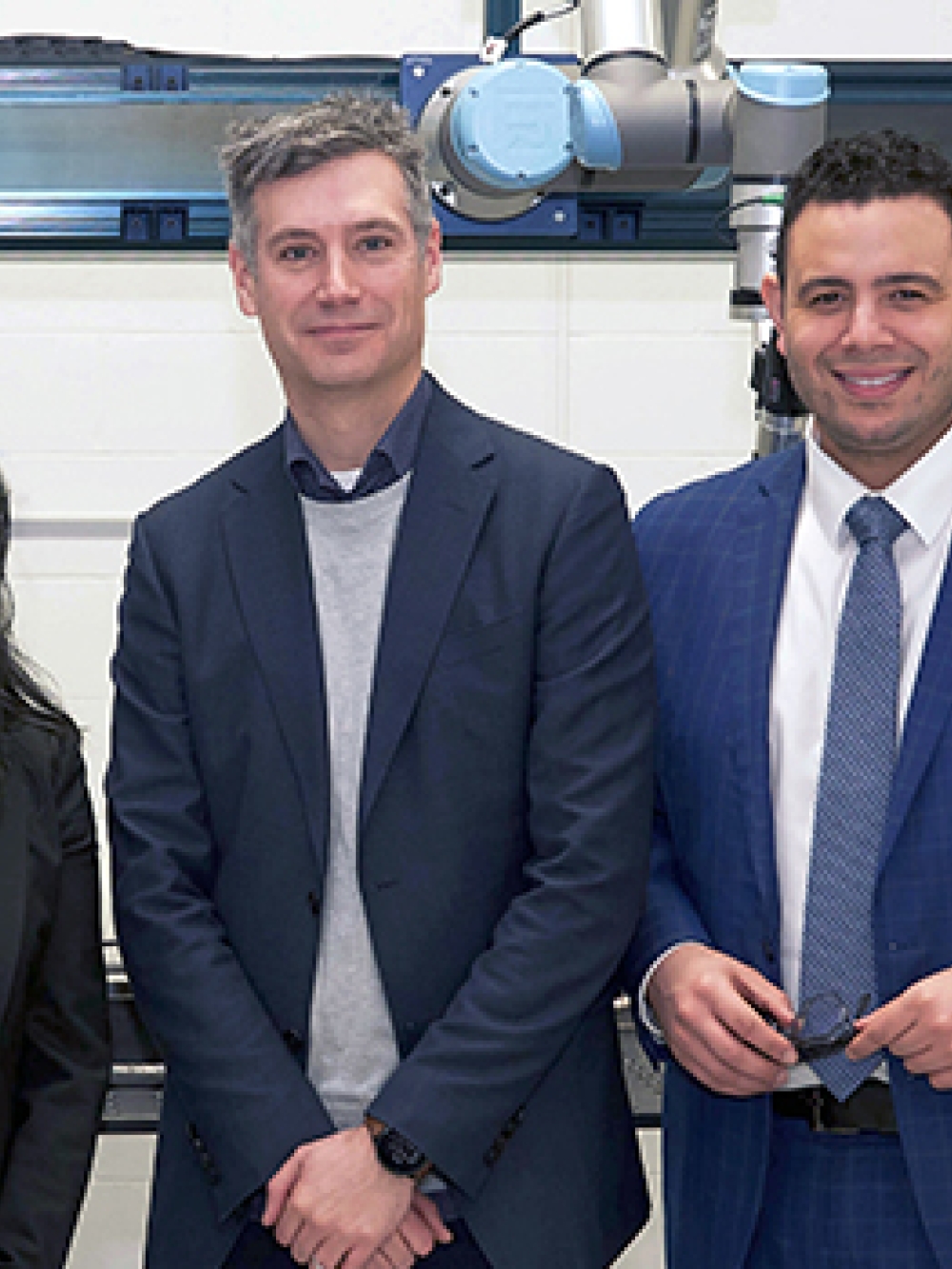 Trois personnes debout dans un environnement industriel, devant un équipement automatisé composé d’une structure métallique, de capteurs et d’un bras robotisé. 