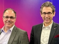 Deux personnes debout, vêtues de vestons professionnels.