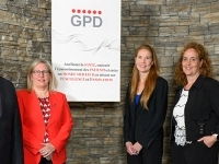 Groupe de personnes debout devant un mur de pierre, posant à côté d’une affiche du Groupe pharmaceutique Duchesnay portant le logo GPD.